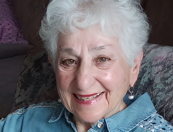 Close up of a woman with short, white hair smiling while sheet sits in an armchair